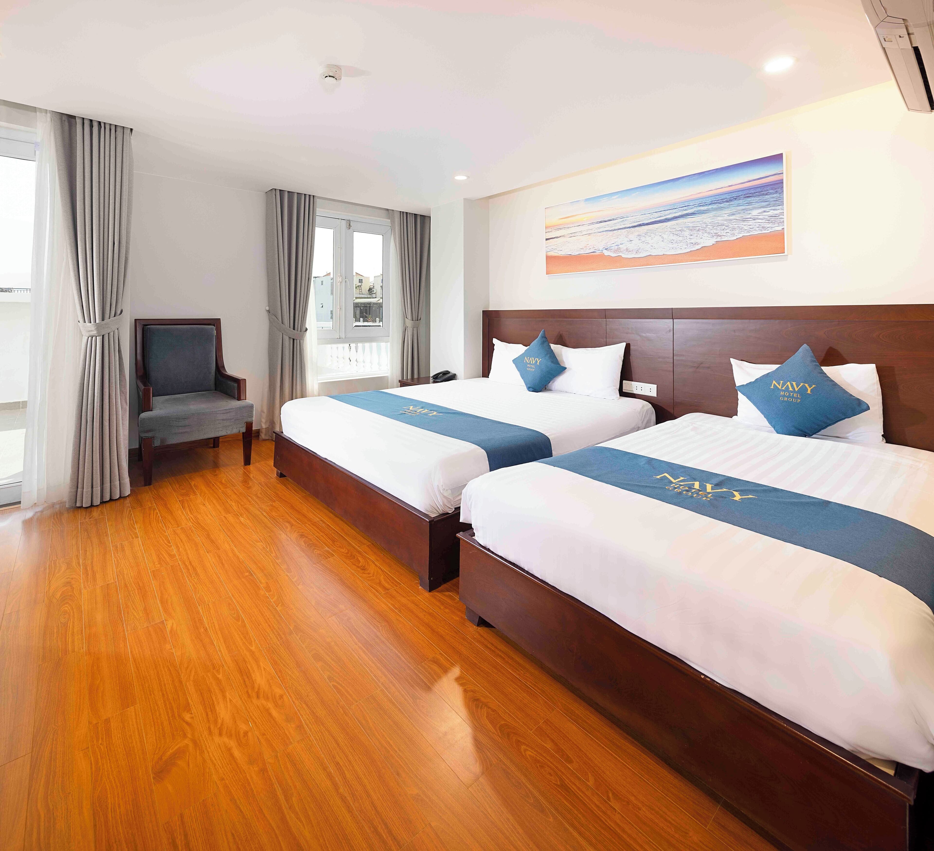 A hotel room with two beds, a wooden floor, a television, and a painting on the wall.