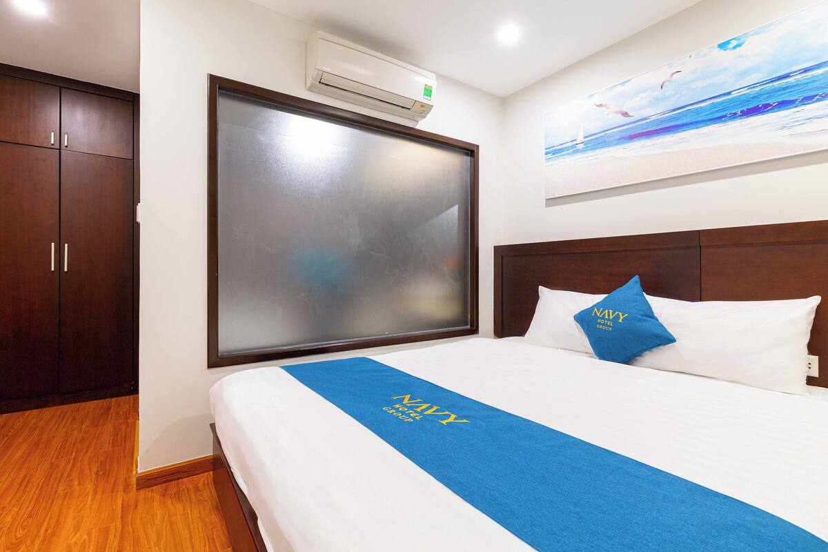 Een hotelkamer met een groot bed, een houten garderobe, een wandairconditioner en een schilderij van een zeegezicht.