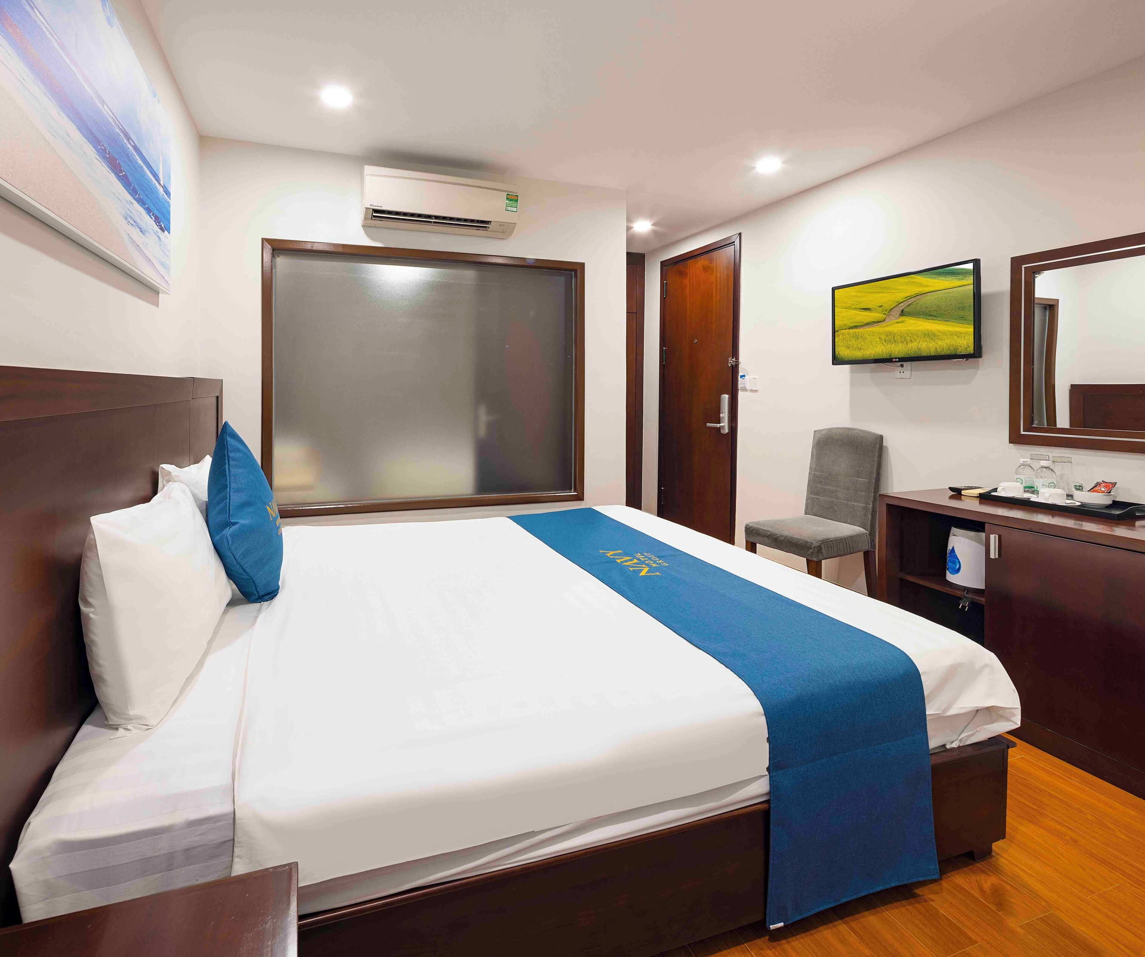 A hotel room with a bed, a desk, a chair, a TV, and a wardrobe.