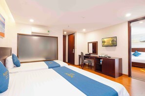Two beds with matching bedding, a desk, and a large window offering a view of the outdoors.