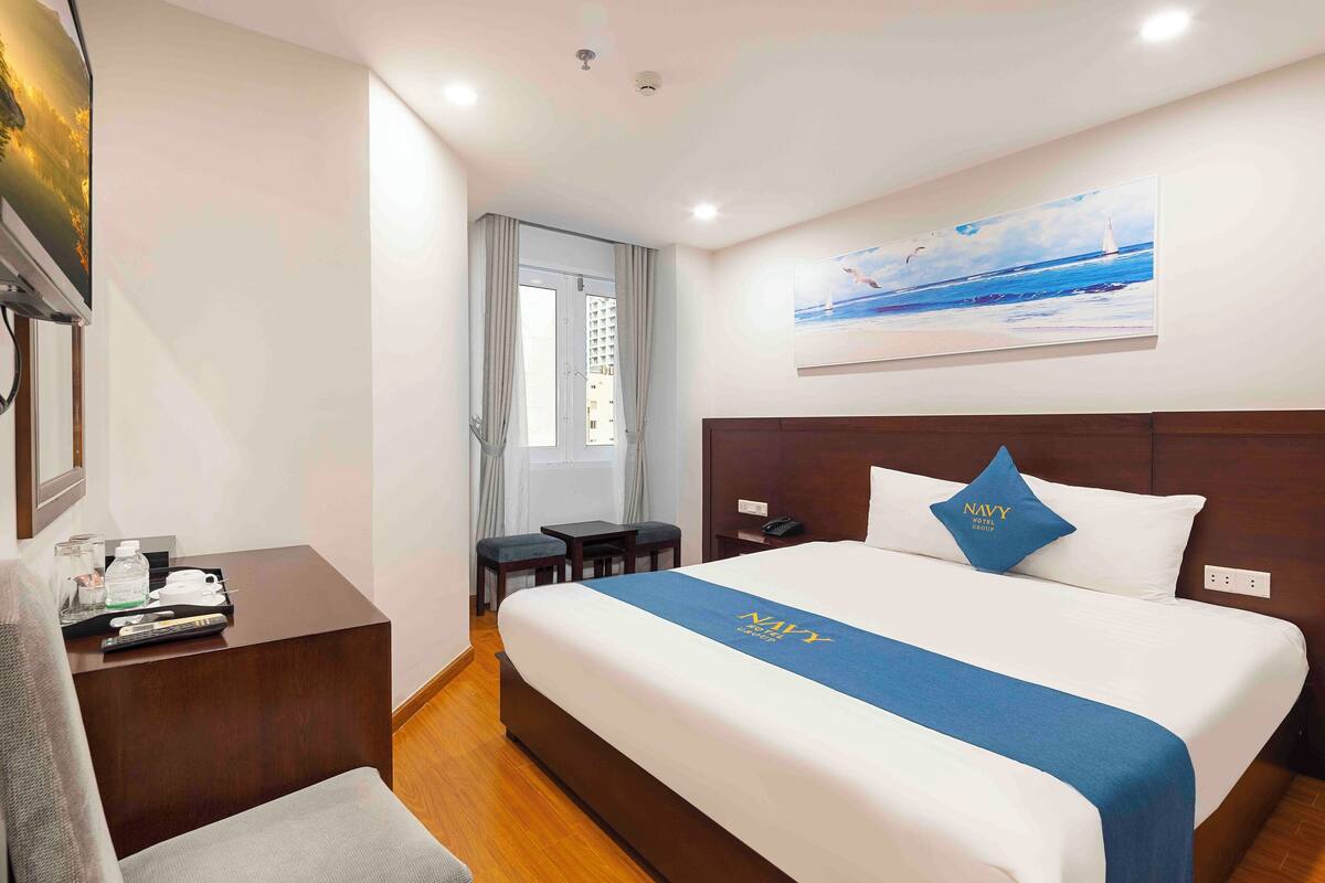 Een hotelkamer met een bed, een bureau, een stoel, een raam met gordijnen en een schilderij aan de muur.