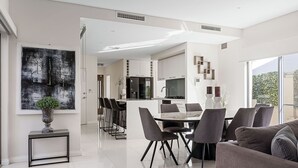 A modern kitchen with a central island, a dining area with a marble table, and a living room with a sofa. - Modern Port Coogee Luxury Home (North Coogee)