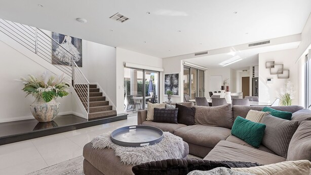 A modern living room with a staircase, a dining area, and a kitchen in the background. - Modern Port Coogee Luxury Home (North Coogee)