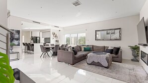 A spacious living area with a large sofa, a dining table, and a kitchen in the background. - Modern Port Coogee Luxury Home (North Coogee)
