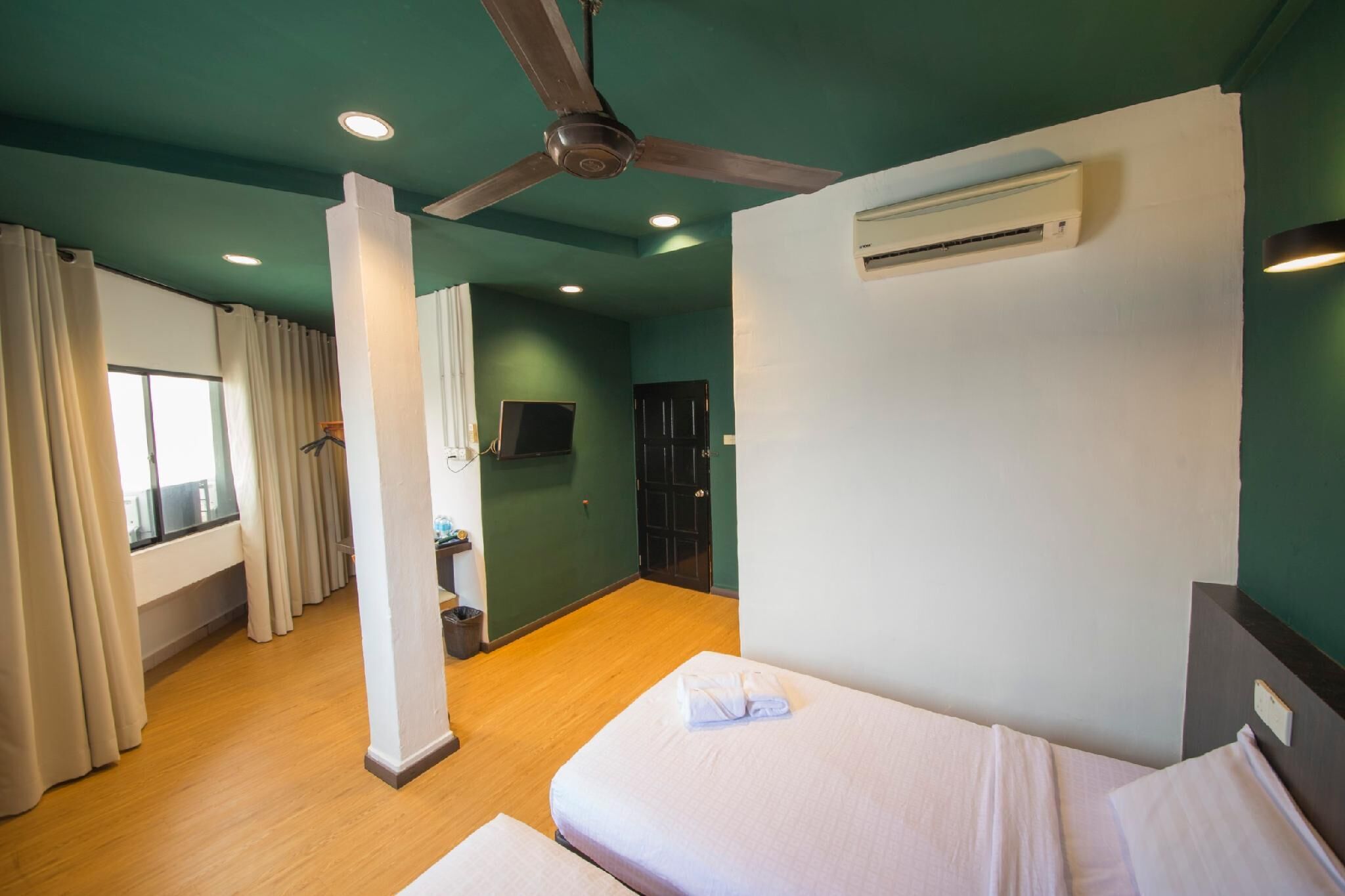 Habitación de hotel con dos camas, ventilador de techo, equipo de aire acondicionado y ventana con cortinas.