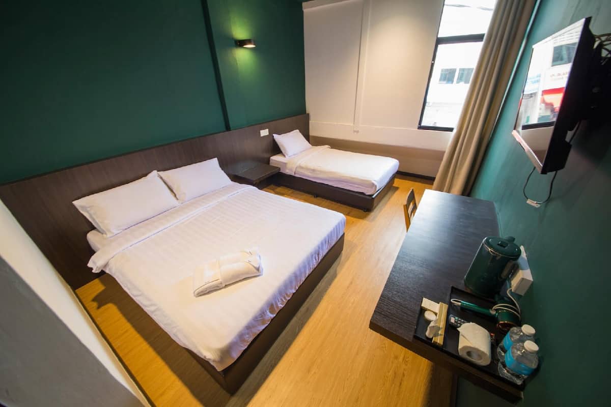 A hotel room with two single beds, a wooden floor, a small table with toiletries, and a window with curtains.