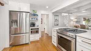 Una cocina moderna con electrodomésticos de acero inoxidable, armarios blancos y piso de madera.