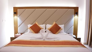 Habitación de hotel con una cama, decoración de toalla en forma de corazón, dos almohadas y cabecera de madera.