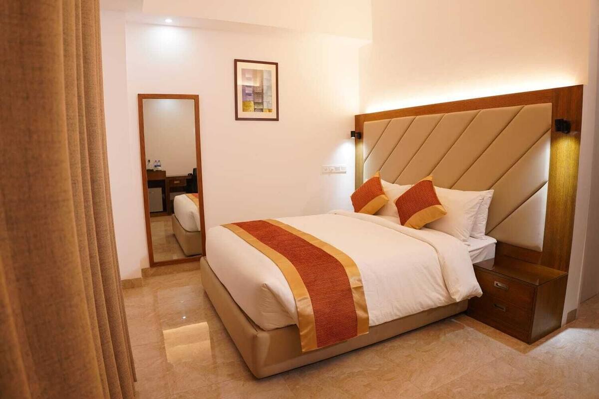 A hotel room with a bed, a nightstand, a mirror, and a framed picture on the wall.