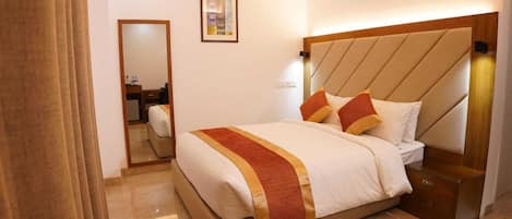 A hotel room with a bed, a nightstand, a mirror, and a framed picture on the wall.