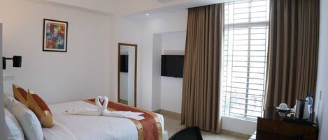 A hotel room with a bed, a desk, a chair, a TV, and a window with curtains.