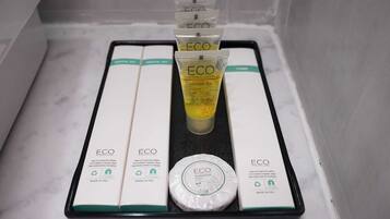 Un bagno con un piano lavabo in marmo bianco, un vassoio nero che contiene una confezione di gel doccia, una saponetta e due scatole etichettate 'ECO'.