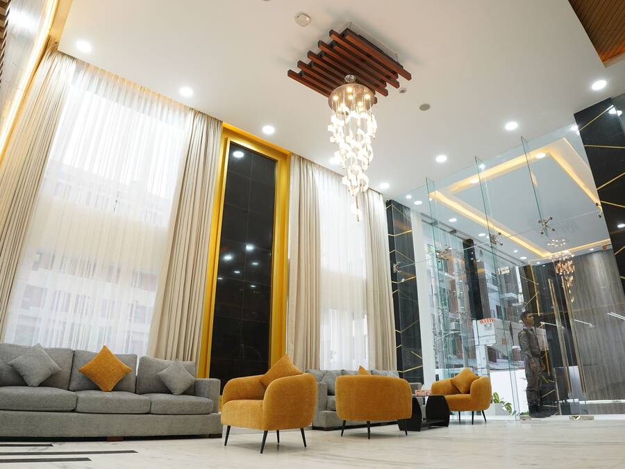A modern lobby with a grey sofa, two yellow armchairs, and a chandelier.