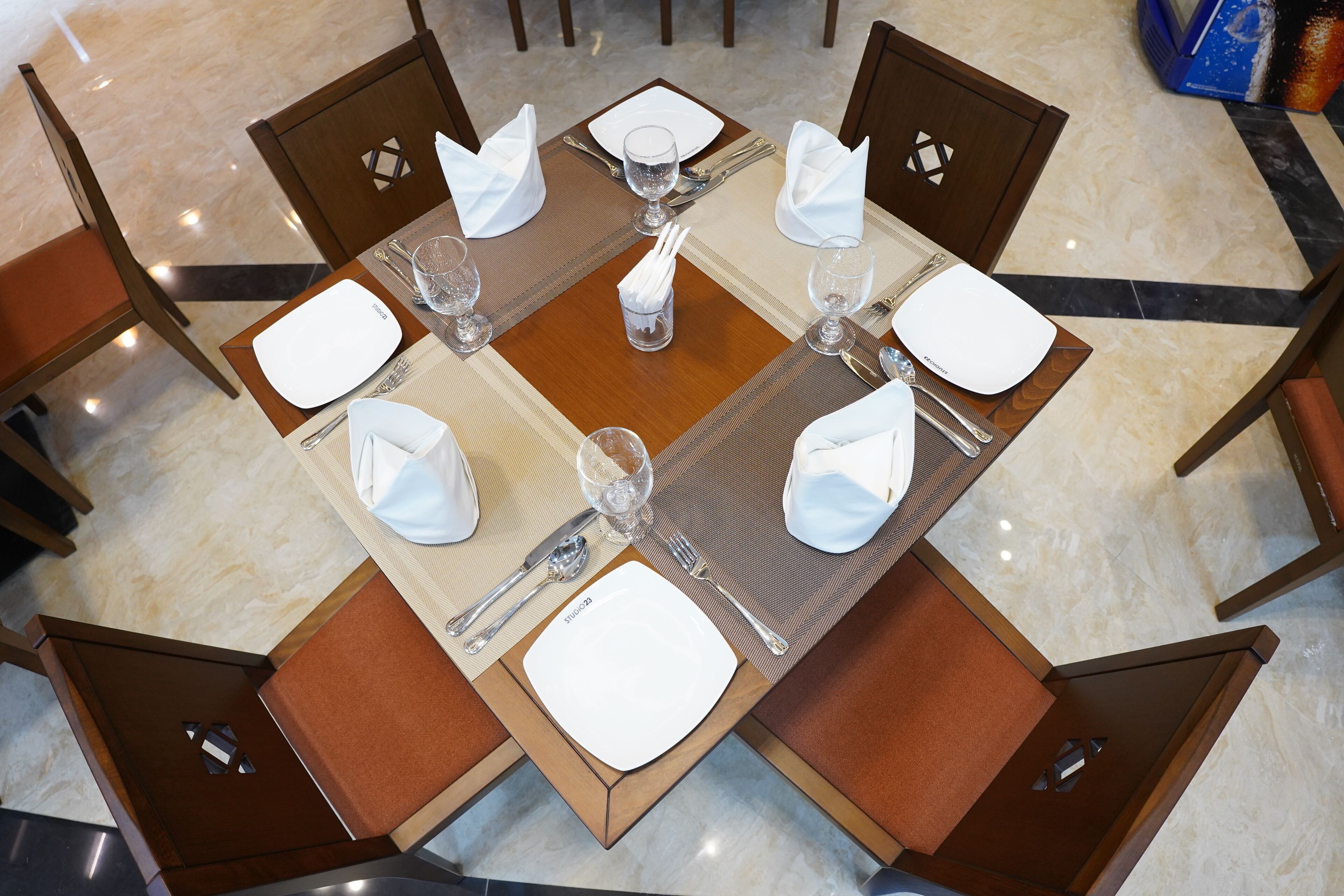 A dining table set for four with a square placemat, white napkins, and silverware.