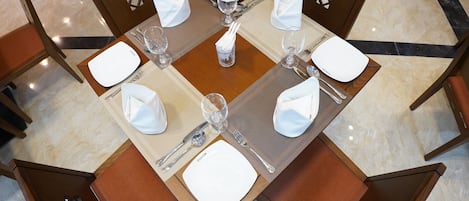 Une table à manger dressée pour quatre personnes, avec un set de table carré, des serviettes blanches et des couverts en argent.