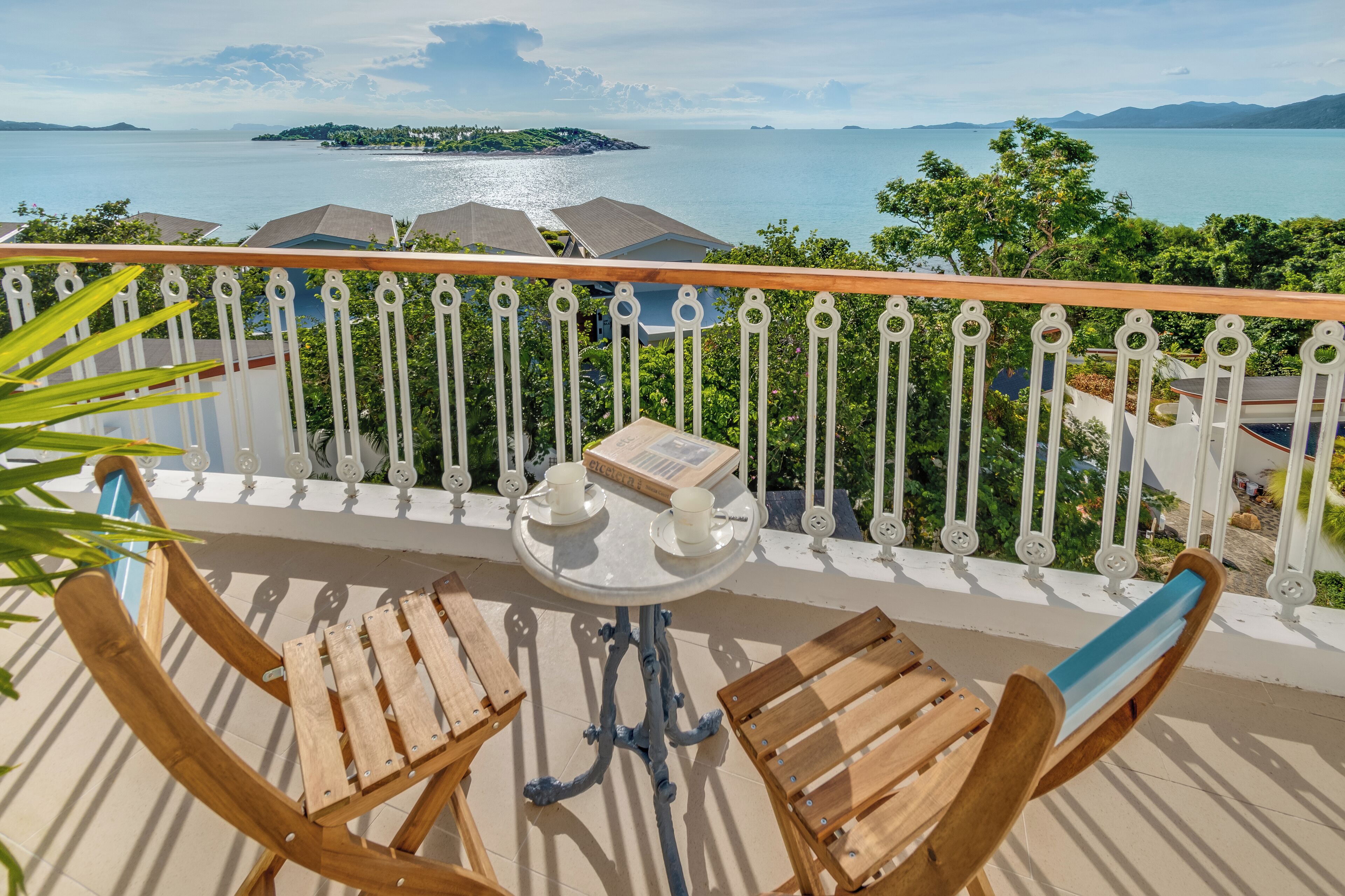 A balcony with two wooden chairs and a small table, overlooking a body of water and distant land.