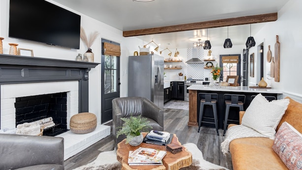 Una sala de estar moderna con chimenea, sofá de cuero y un comedor con taburetes de bar.