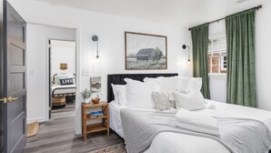 Un dormitorio con una cama grande, una mesita de noche con una lámpara, un cuadro en la pared y vistas a una cortina verde.