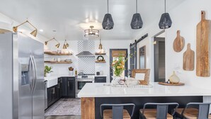 Una cocina moderna con una isla central, taburetes de bar, iluminación colgante y tablas de cortar de madera en la pared.