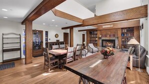 A spacious living room with a large wooden dining table, comfortable seating, a fireplace, and a bookshelf filled with books. - Downtown 3BR Park City Retreat: Walk to Town Lift (Park City)