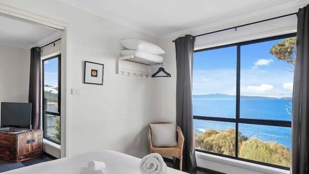 Een hotelkamer met een groot bed, een televisie, een stoel en uitzicht op zee.