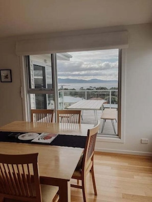 Zona pranzo con tavolo e sedie, vista sull'esterno tramite ampie finestre e un balcone con tavolo e sedie.