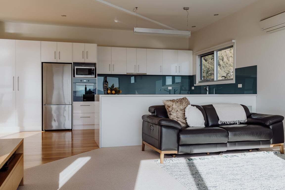 A modern kitchen with white cabinets, a black leather sofa, and a window.