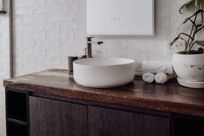 Une salle de bain avec un lavabo blanc, un meuble-lavabo en bois foncé et une plante en pot.