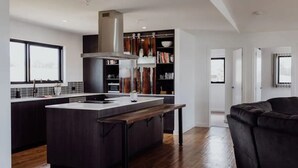 A modern kitchen with a central island, dark cabinetry, and a large window. - Bayview Lodge - Views Views Views! (Break O'Day)