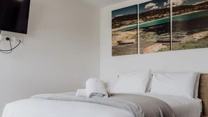 A neatly made bed with white linens and a gray throw blanket, a wooden headboard, and a wall-mounted flat-screen TV. - Bayview Lodge - Views Views Views! (Break O'Day)