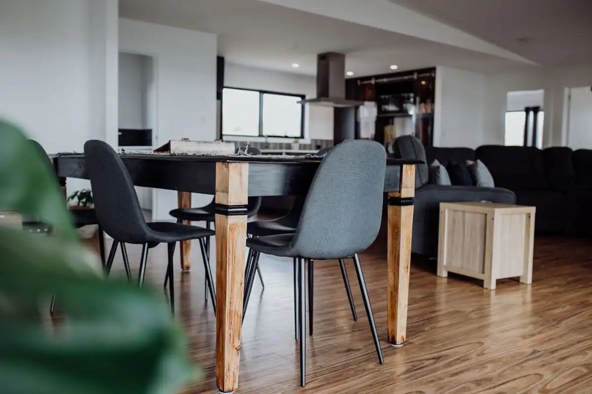 Una sala de estar moderna con un sofá negro, una mesa de comedor con sillas y una pequeña mesita de madera.