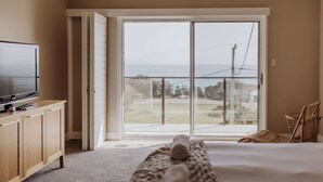 A bedroom with a large sliding glass door leading to a balcony, a bed, a TV on a wooden cabinet, and a wicker chair. - Haven on James - Luxurious Ocean Vista (Glamorgan-Spring Bay)