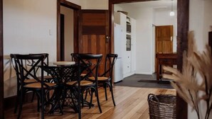 Zona pranzo con tavolo e sedie in legno, una cucina sullo sfondo e un cesto di vimini sul pavimento.