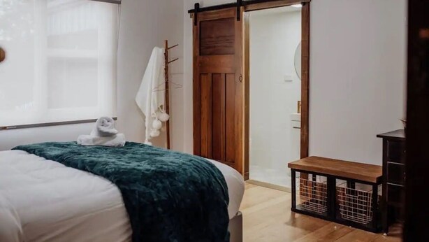 Una camera da letto con un letto, una porta in legno, una panca e una finestra con tenda.