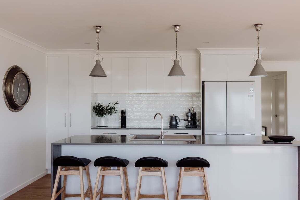 A modern kitchen with white cabinetry, a central island with bar stools, pendant lighting, and a stainless steel refrigerator.