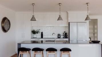 A modern kitchen with white cabinetry, a central island with bar stools, pendant lighting, and a stainless steel refrigerator.