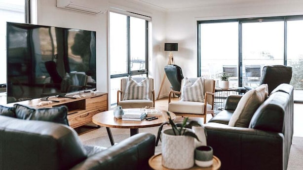 A modern living room with a large flat-screen TV, comfortable seating, and large windows offering a view of the outdoors. - Anchored@Bicheno - Ohmyview! (Glamorgan-Spring Bay)