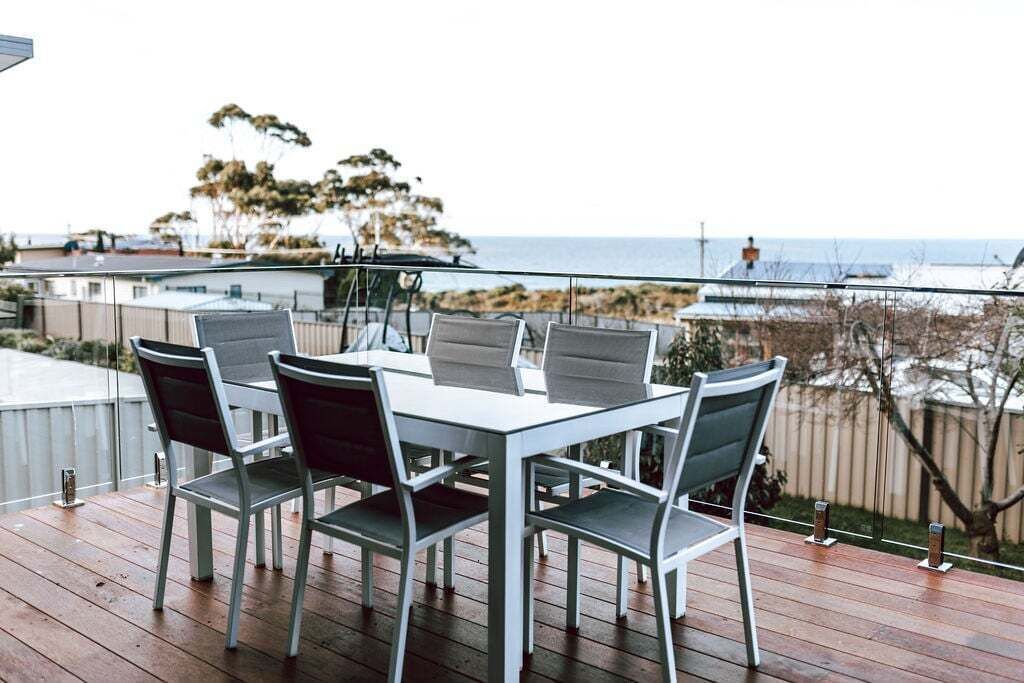 A deck with a table and chairs, overlooking a beach and ocean.