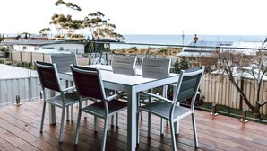 A deck with a table and chairs, overlooking a beach and ocean. - Anchored@Bicheno - Ohmyview! (Glamorgan-Spring Bay)