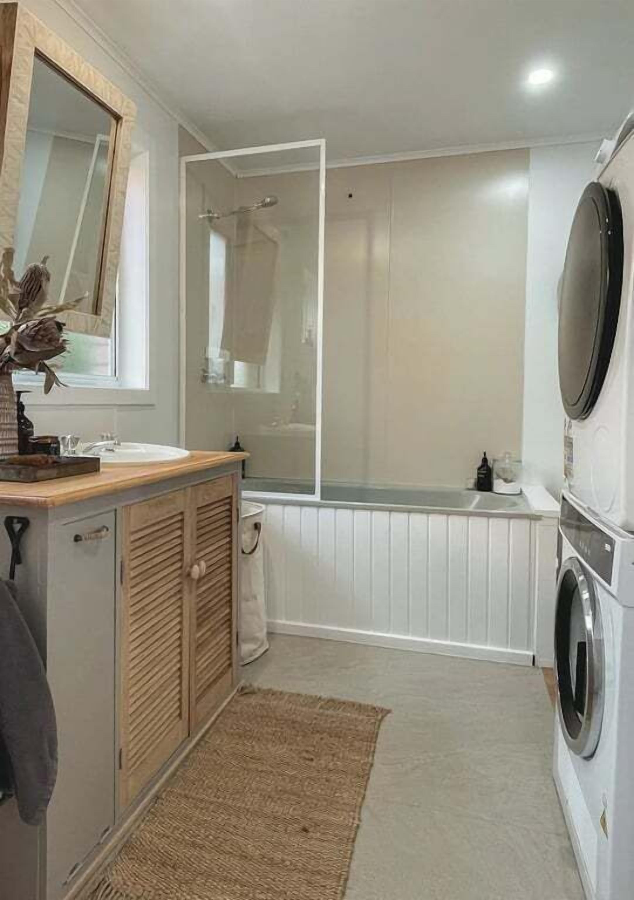 A compact laundry room with a washing machine, a sink, and a mirror.