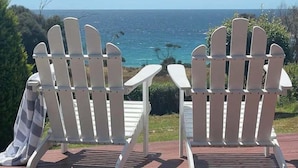 Two Adirondack chairs facing a view of the ocean.