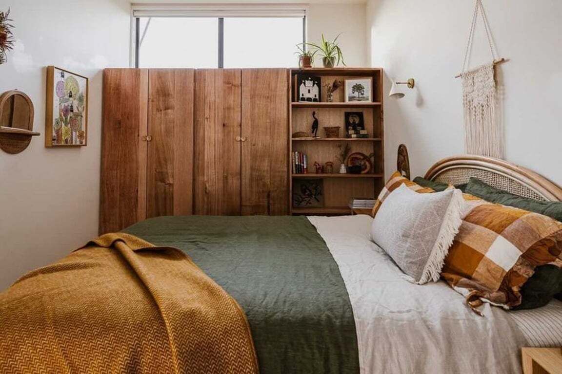Un dormitorio con cama, armario de madera, estantes con objetos decorativos y un tapiz de macramé.