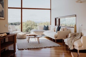 A spacious living room with a large window, a sofa set, a coffee table, and a wooden side table.