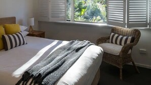A bedroom with a bed, a chair, a window with shutters, and a ceiling fan.