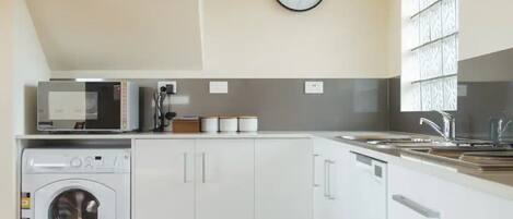 Una cocina compacta con lavadora, microondas y un reloj en la pared.