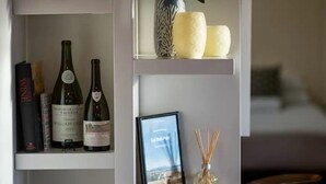 Una estantería con libros, botellas de vino, un florero con flores, velas y un cuadro enmarcado.