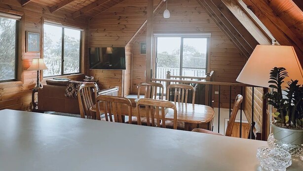 A cozy wooden cabin with a dining area, a TV, and a balcony with a railing. - Barefoot Bungalow | Cozy Bicheno Hideaway | (Glamorgan-Spring Bay)