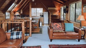A cozy cabin interior with a dining area, kitchen, and a living room with a fireplace. - Barefoot Bungalow | Cozy Bicheno Hideaway | (Glamorgan-Spring Bay)