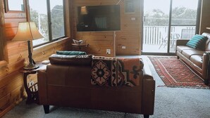 A cozy room with a wooden interior, a sofa, a TV, and a view through large windows. - Barefoot Bungalow | Cozy Bicheno Hideaway | (Glamorgan-Spring Bay)