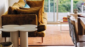 A cozy living room with a sofa, a coffee table, and a view of green hills through a sliding door. - Frankie Beach House Bicheno (Glamorgan-Spring Bay)